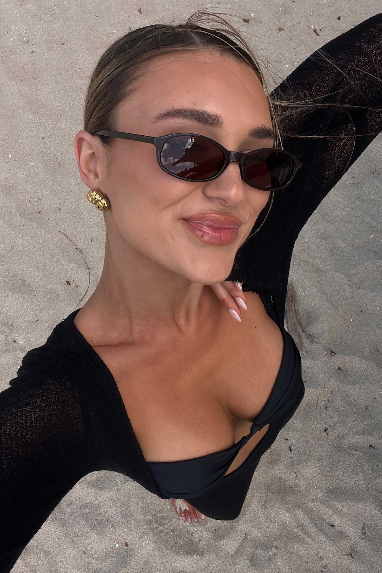 Woman wearing sunglasses and a black top on a sandy background