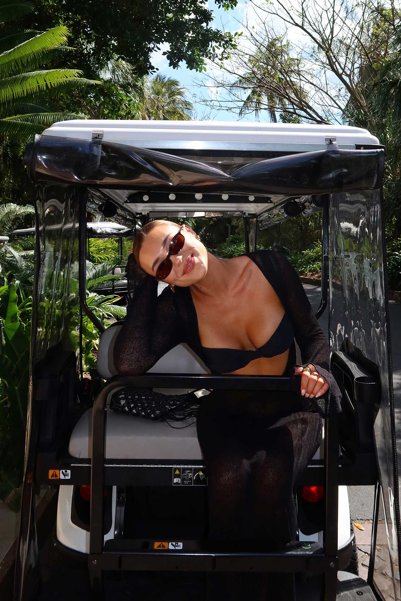 Person sitting in a golf cart with a scenic background of trees and sky.