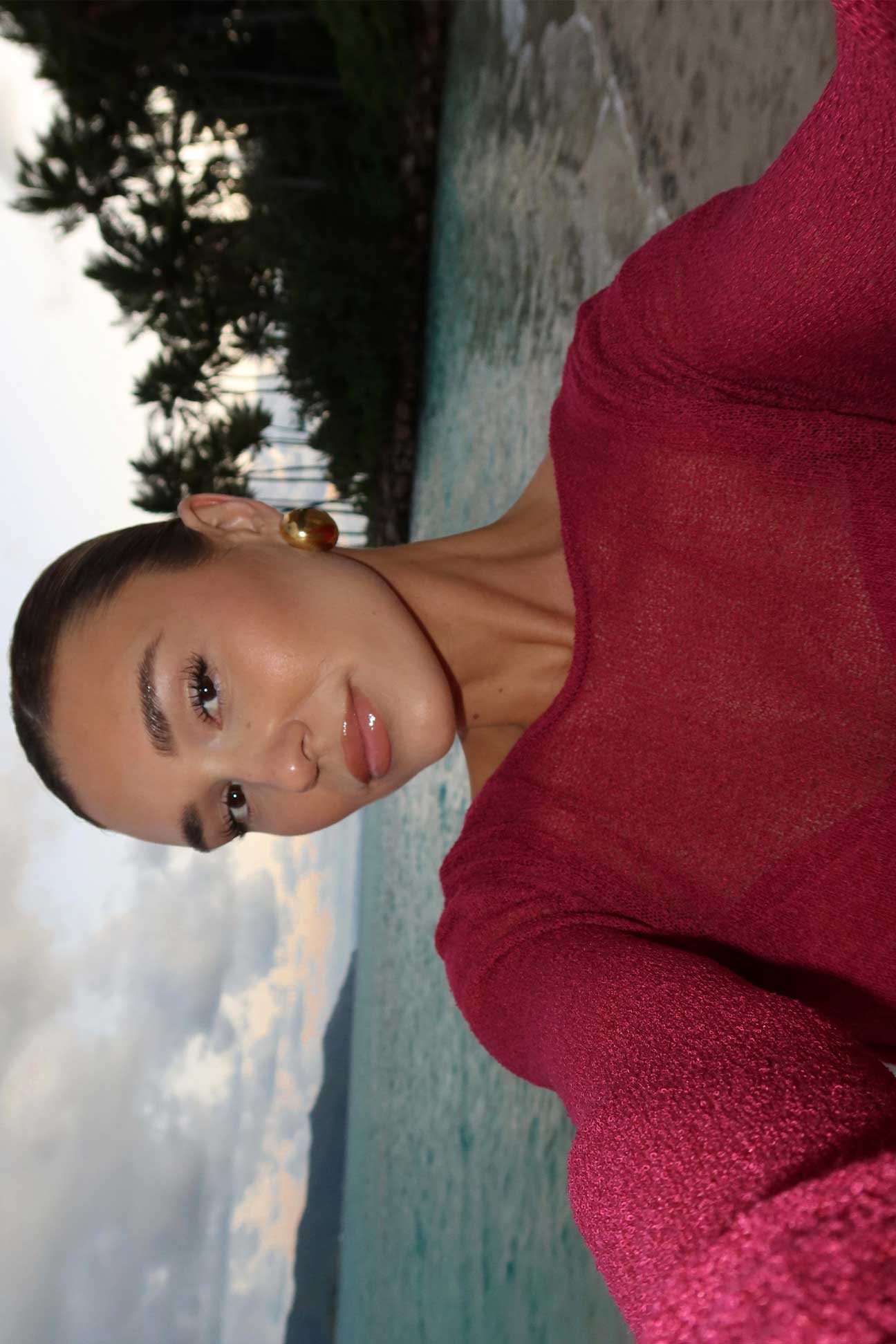 Woman in a magenta dress standing by a pool with trees in the background
