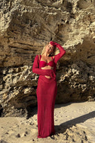 Woman in a magenta dress standing against a rocky wall.