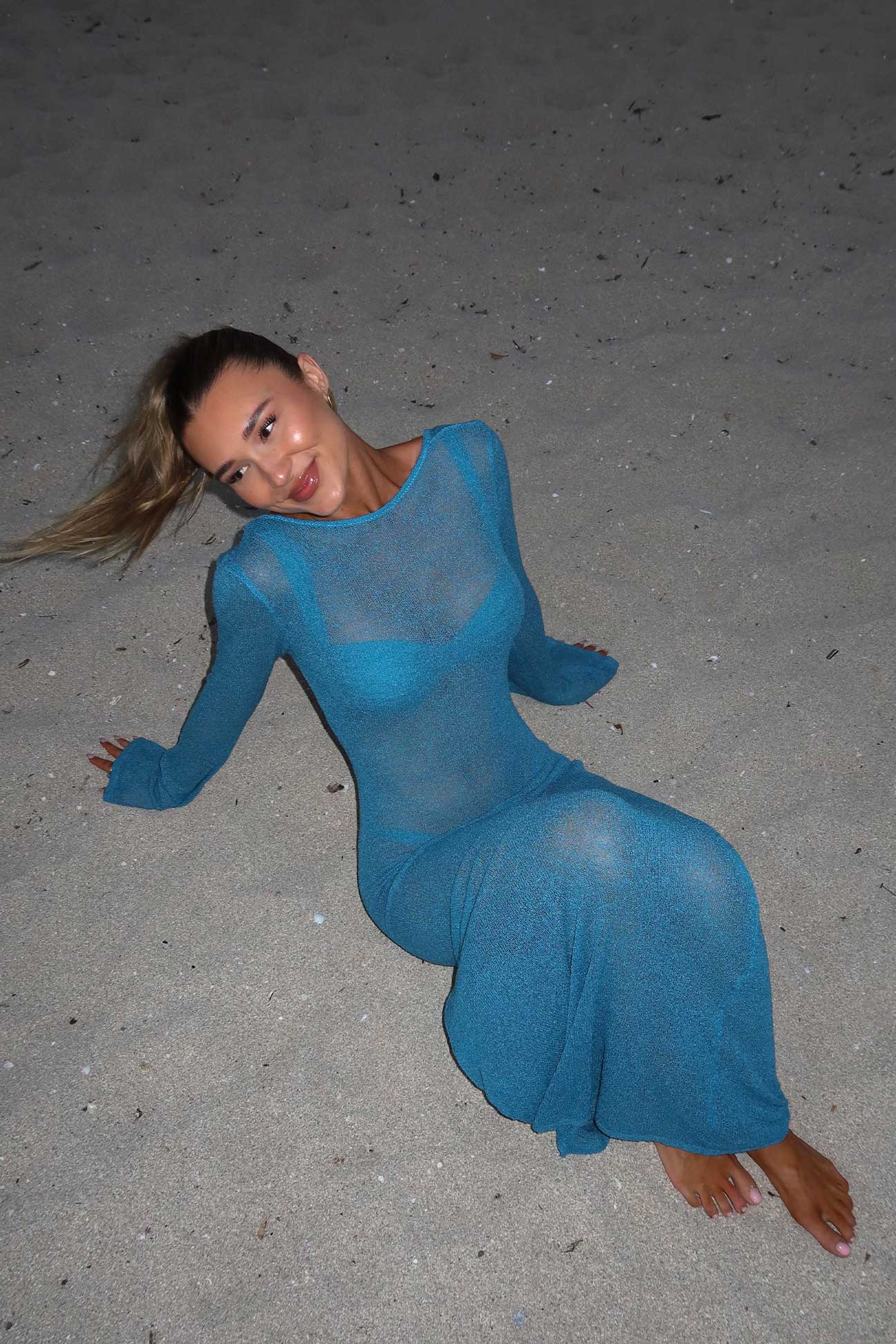 Woman in a blue dress sitting on a sandy surface
