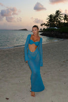 Woman in a teal dress standing on a beach with palm trees and ocean in the background
