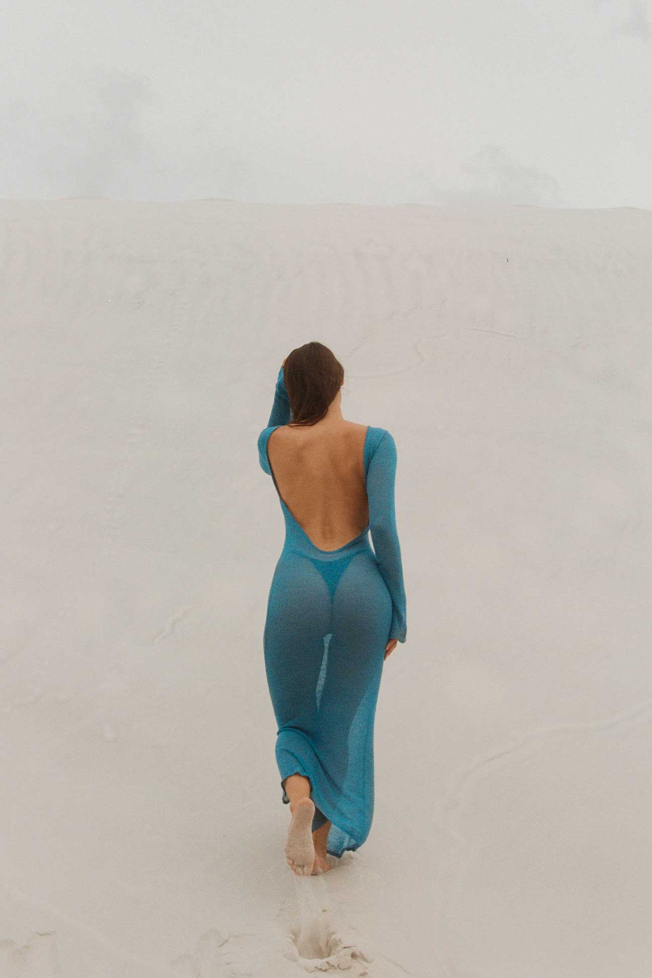 Person wearing a teal dress with a backless design on a plain background