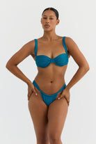 Woman wearing a teal bikini against a white background