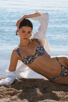 Woman in a blue floral bikini lying on the beach with a white shirt.
