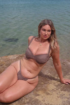 Woman in a brown bikini sitting on a rock by the water