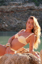 Woman in a soft yellow bikini sitting on rocks with a scenic background
