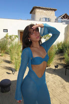 Woman in a teal outfit standing outdoors with a building in the background