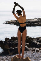 Person in a black swimsuit standing on rocks by the water