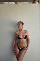 Woman wearing a black bikini against a plain wall
