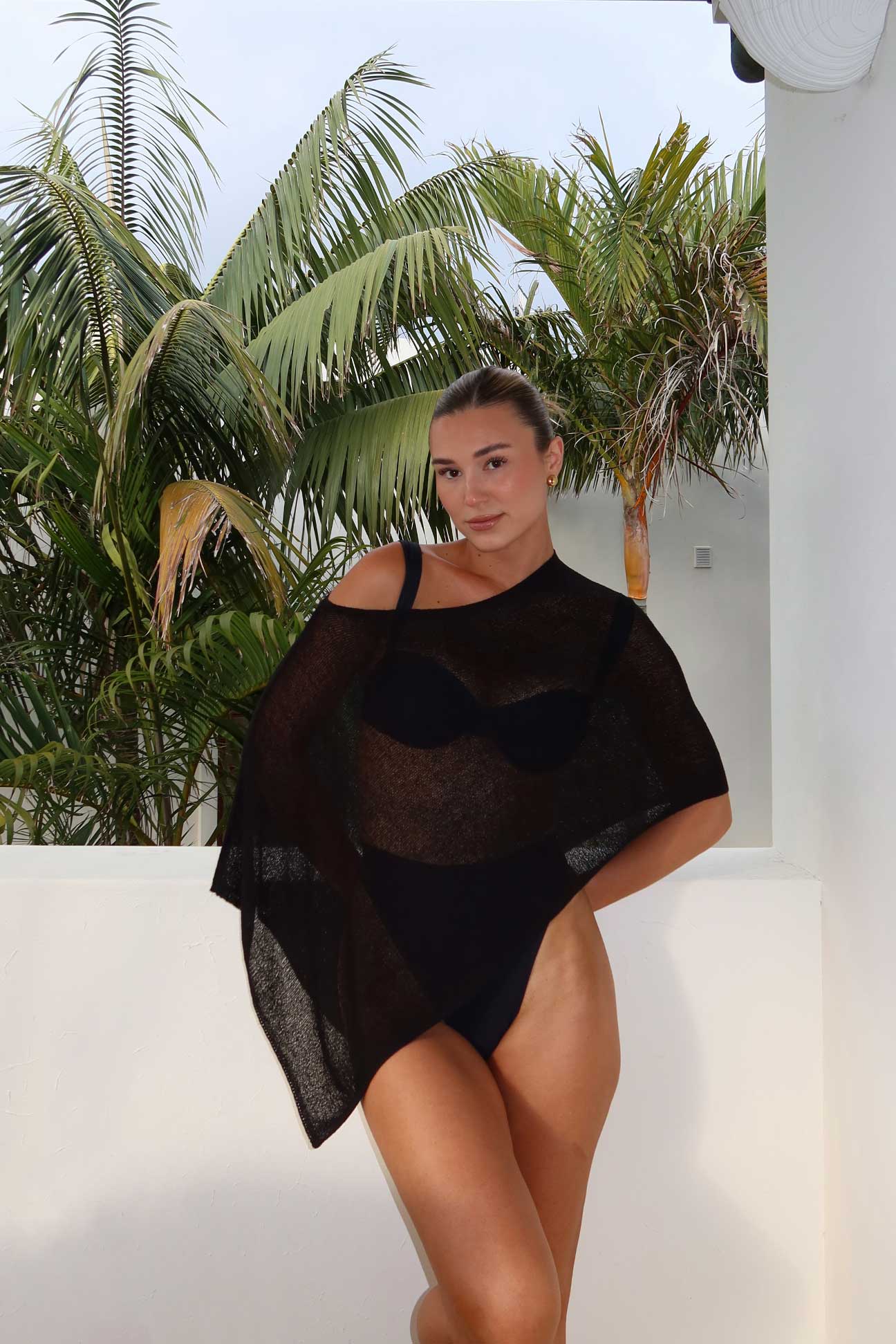 Person wearing a black outfit with sheer details against a tropical background