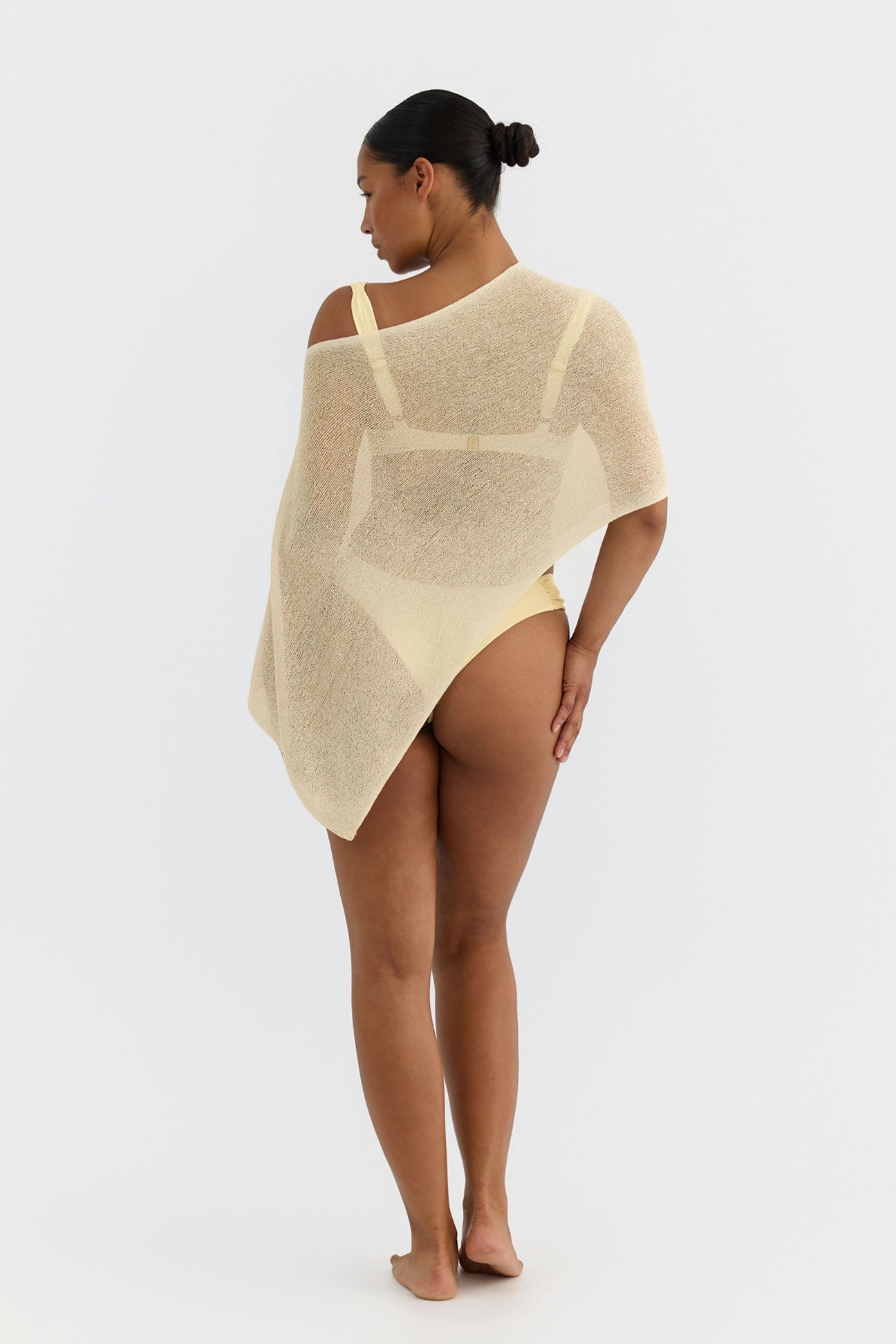 Woman wearing a butter yellow knit poncho on a white background