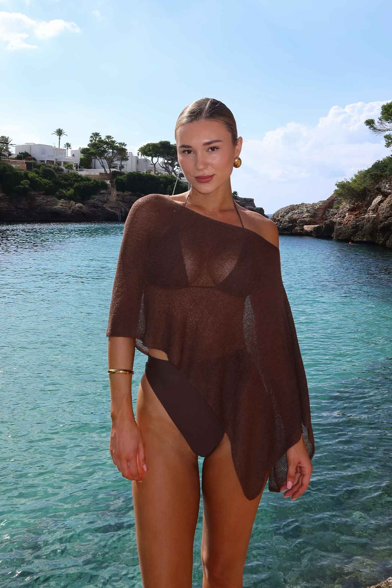 Woman in a brown swimsuit standing by a body of water with a scenic background