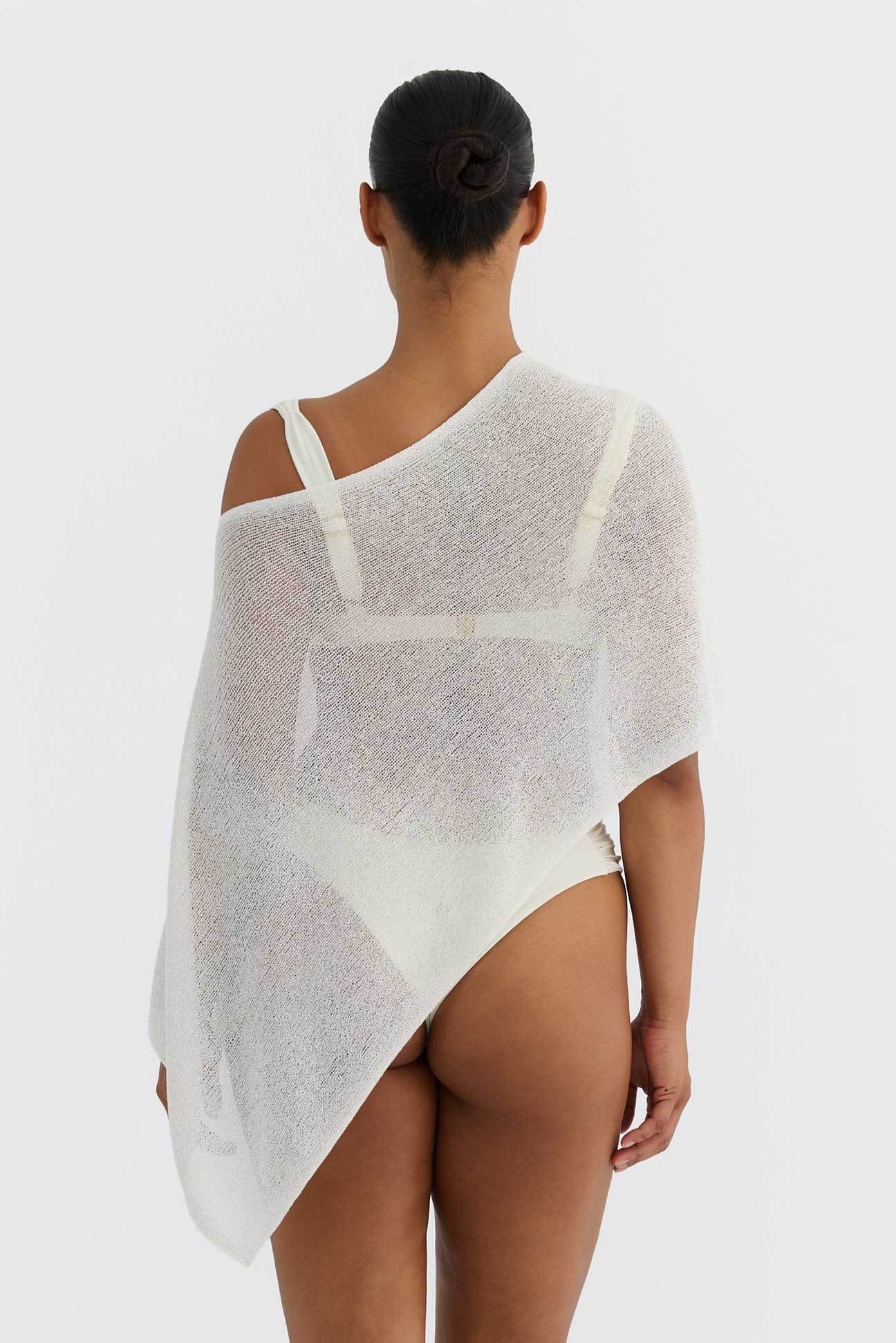 Person wearing a sheer white top with thin straps on a plain background