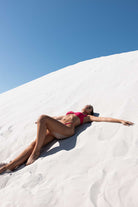 Person in a pink bikini lying on a white sand dune with clear blue sky
