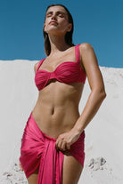 Woman wearing a pink bikini and sarong against a white wall and blue sky.