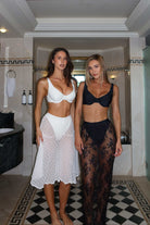 Two women in bikinis standing in a bathroom with decorative tiles.