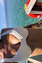 Person wearing a white bikini top by a pool with clear blue water.