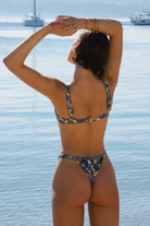 Woman in a floral bikini standing by the water with boats in the background
