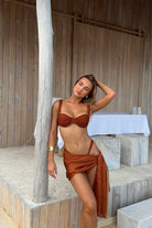 Woman in a terracotta bikini standing against a wooden wall.