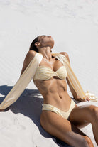 Woman in a beige bikini lying on a sandy beach with a white towel draped over her.