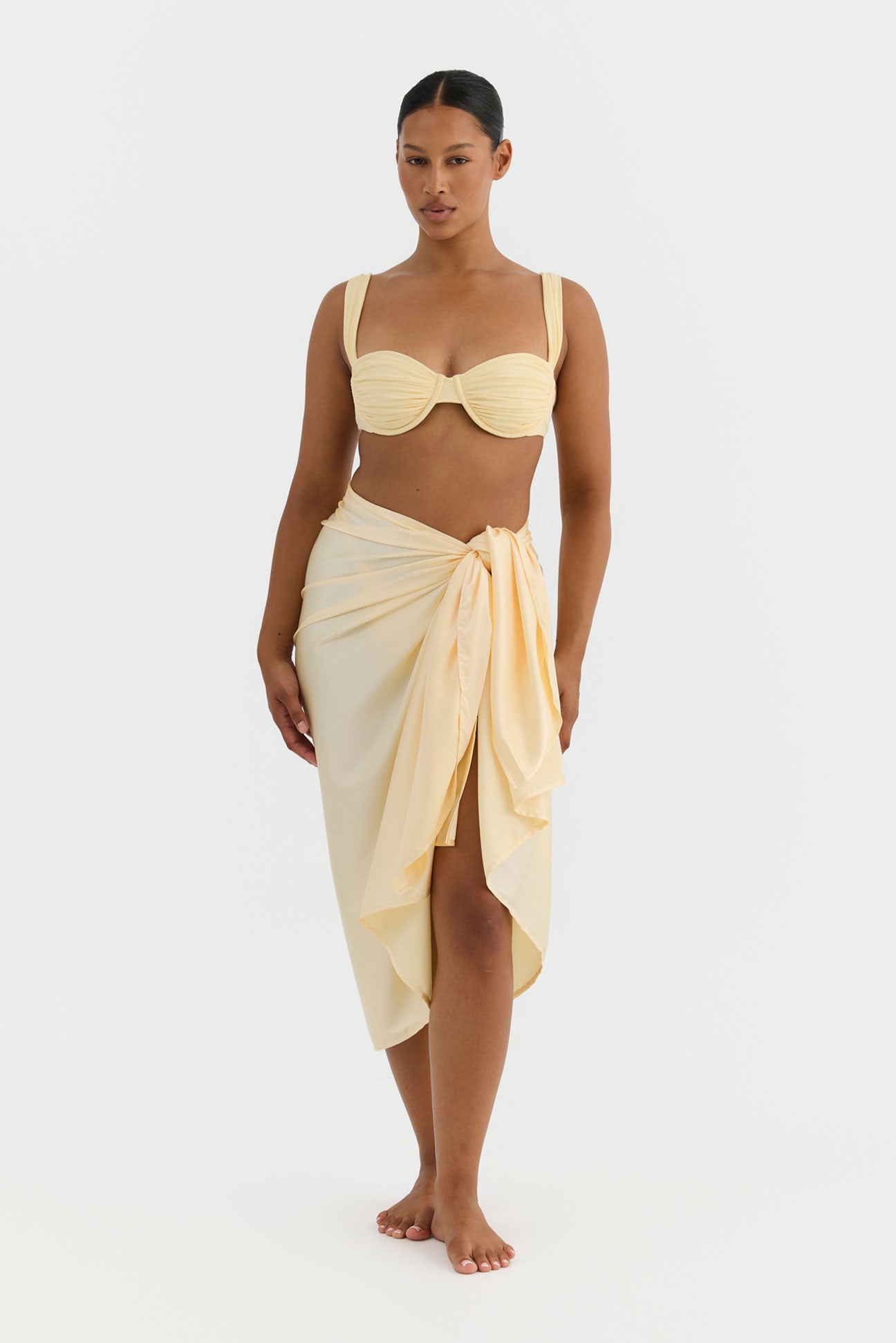 Woman wearing a butter coloured bikini top and wrap skirt on a white background