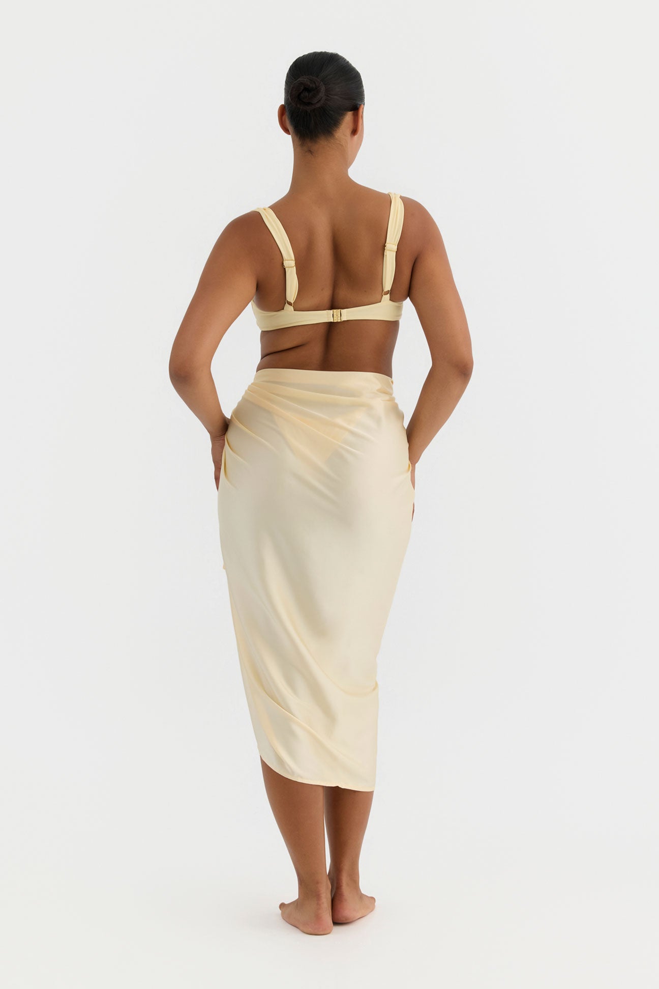 Woman wearing a yellow top and butter skirt on a white background