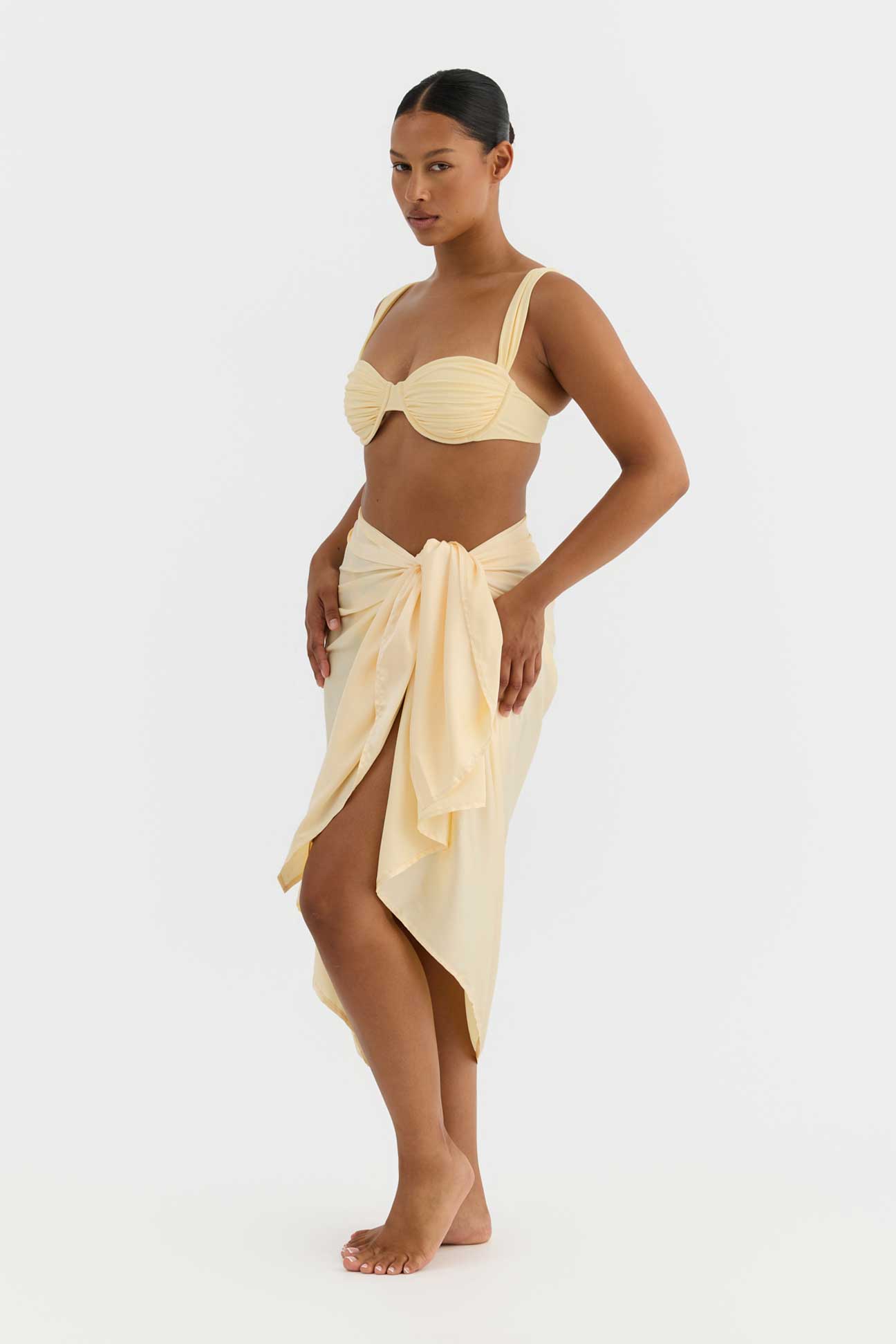 Woman wearing a yellow bikini set with a matching wrap skirt on a white background
