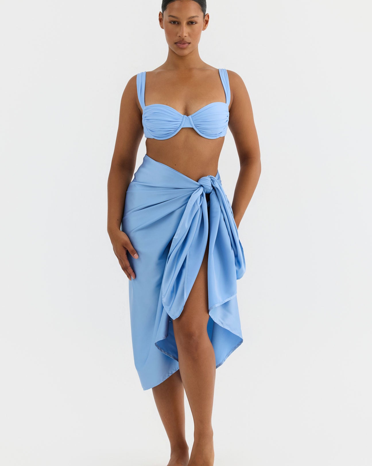 Woman wearing a light blue bikini with a matching sarong on a white background