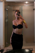 Person taking a mirror selfie wearing a black strapless bikini top and skirt in a bathroom.