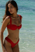 Woman in a red bikini standing on a beach with clear blue water.