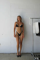 Woman wearing a black bikini standing against a white tiled wall.