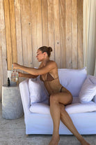 Woman in a brown bikini sitting on a white couch with a wooden wall background