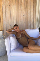 Woman sitting on a white couch with brown bikini on against a wooden wall