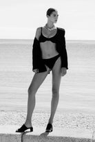 Black and white photo of a woman in a swimsuit and cardigan on a beach.