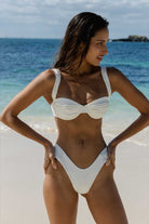 Woman in a white bikini standing on a sandy beach.