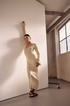 Woman in a beige dress posing in an industrial-style room with large windows.