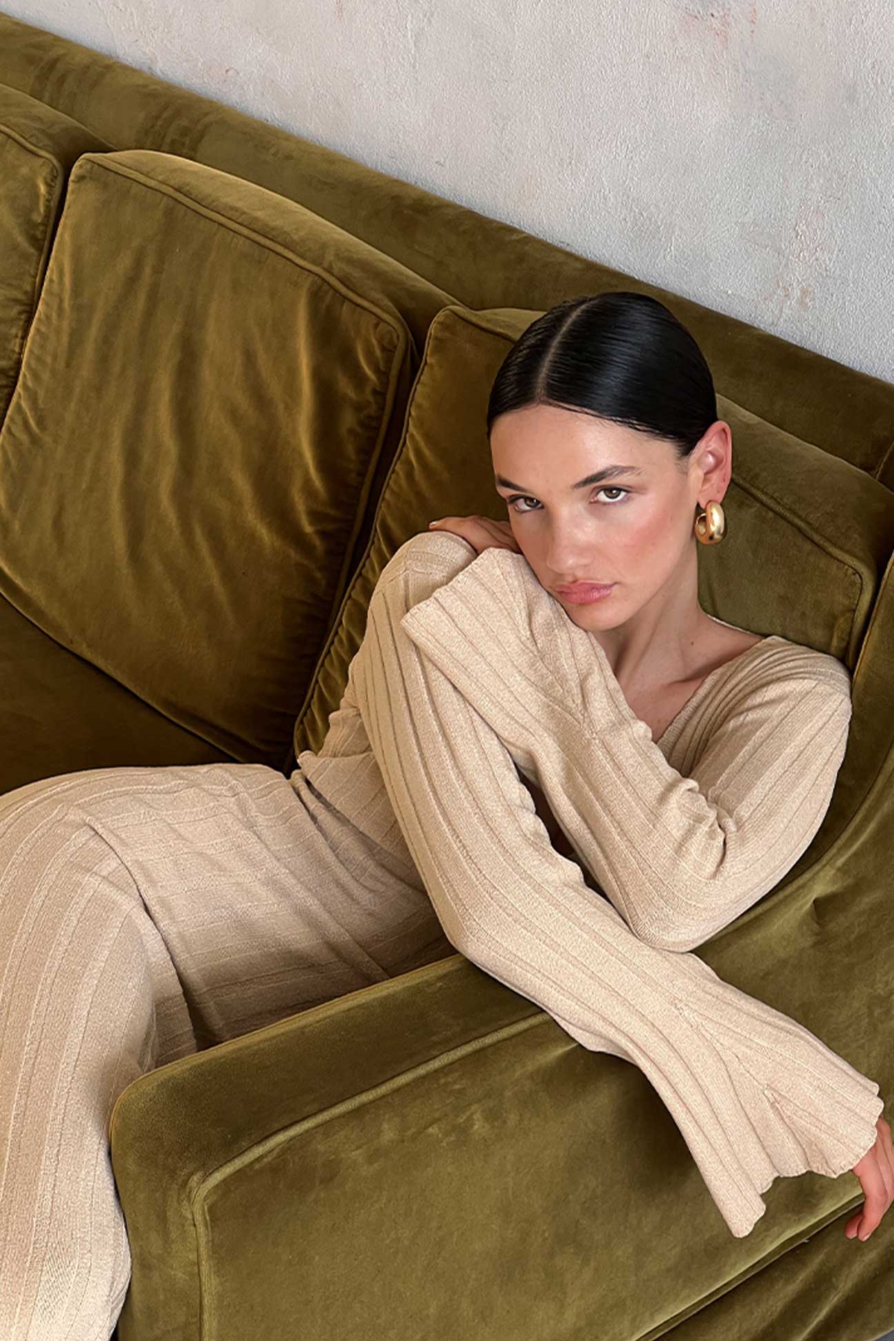 Woman in a beige dress sitting on a green velvet couch.