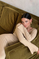 Woman in a beige dress sitting on a green velvet couch.
