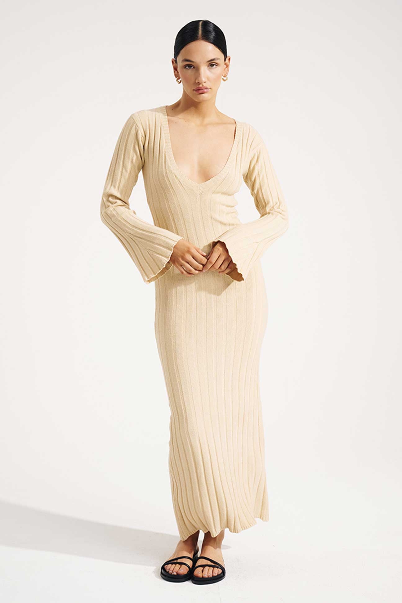 Woman wearing a long, light-colored ribbed dress on a white background