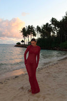 Person in a magenta dress standing on a beach with palm trees and sunset in the background
