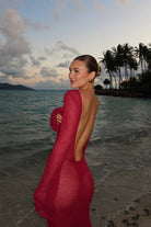 Woman in a magenta dress standing on a beach with palm trees and ocean in the background