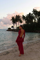 Woman in a magenta outfit standing on a beach with palm trees and water in the background