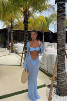 Woman in a blue dress standing in a tropical outdoor setting with palm trees and white furniture.