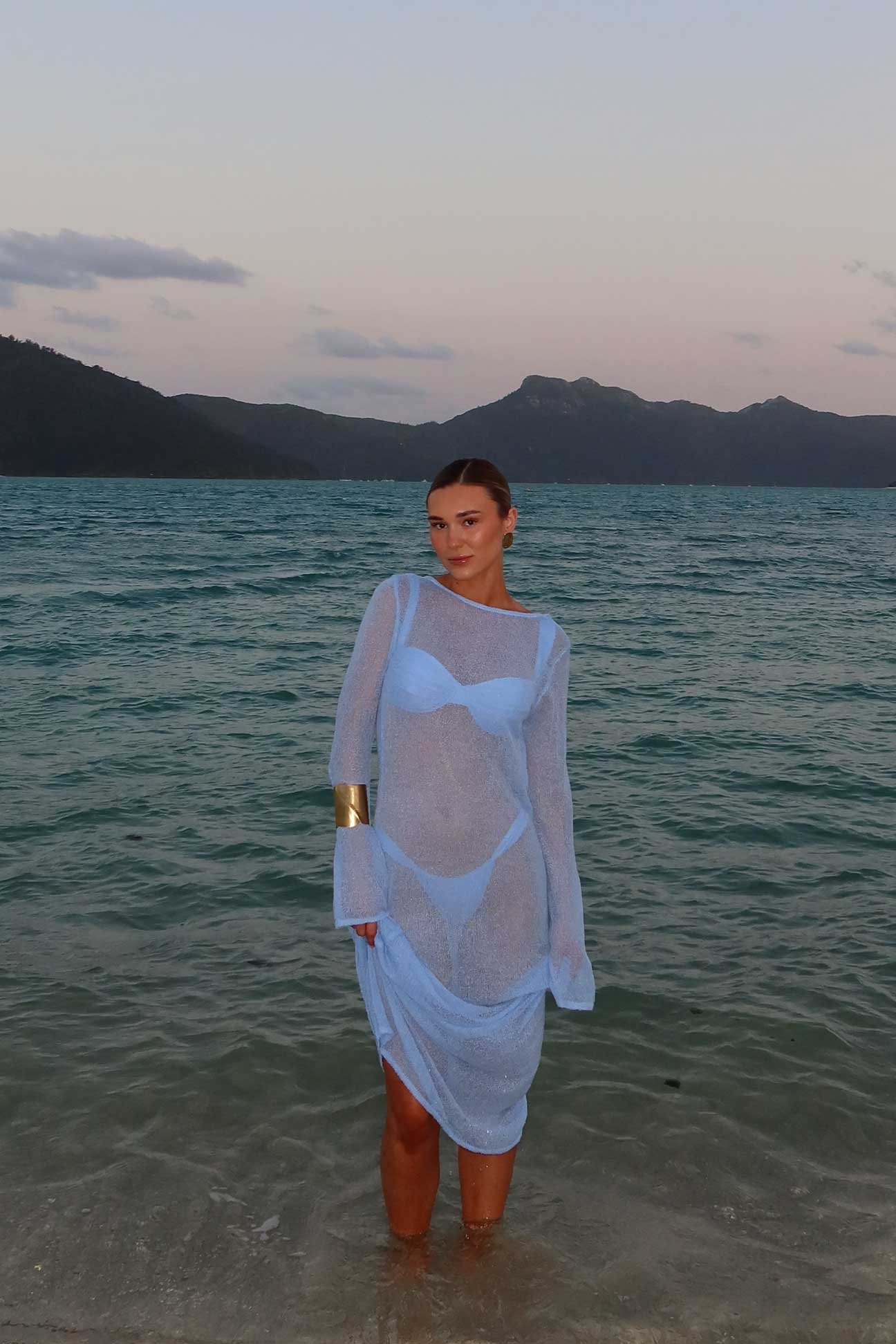 Person standing in water wearing a sheer white dress with mountains in the background