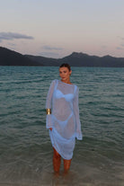 Person standing in water wearing a sheer white dress with mountains in the background
