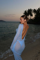 Woman in a light blue dress standing on a beach with palm trees in the background