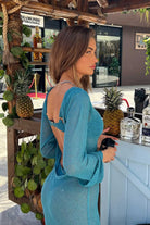 Woman in a blue dress standing behind a bar with decorative elements.