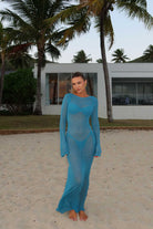 Woman in a blue dress standing on a sandy area with palm trees in the background