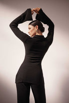 Woman wearing a black ribbed sweater and pants against a neutral background